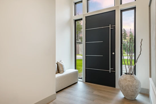 Entr&eacute;e principale d'une maison r&eacute;sidentielle avec double porte en bois brun &agrave; panneaux sur&eacute;lev&eacute;s, encadr&eacute;e par des colonnes blanches cannel&eacute;es sur bases en pierre naturelle multicolore