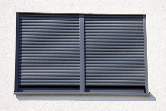 Fa&ccedil;ade ext&eacute;rieure de b&acirc;timent r&eacute;sidentiel en briques oranges avec fen&ecirc;tre &eacute;quip&eacute;e d'un volet roulant blanc partiellement ouvert