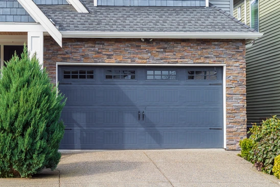 Garage r&eacute;sidentiel avec porte sectionnelle blanche partiellement ouverte, fa&ccedil;ade en bardage bois peint beige, toiture &agrave; pignon avec bardeaux d'asphalte