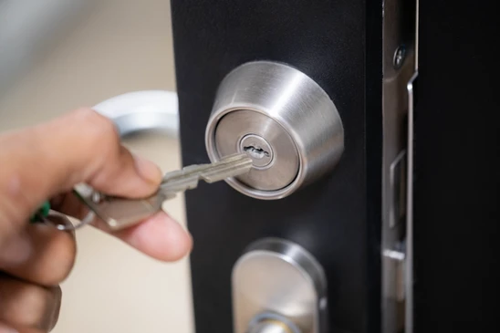 Mains d'un serrurier installant une serrure de porte int&eacute;rieure dans un environnement r&eacute;sidentiel aux murs blancs
