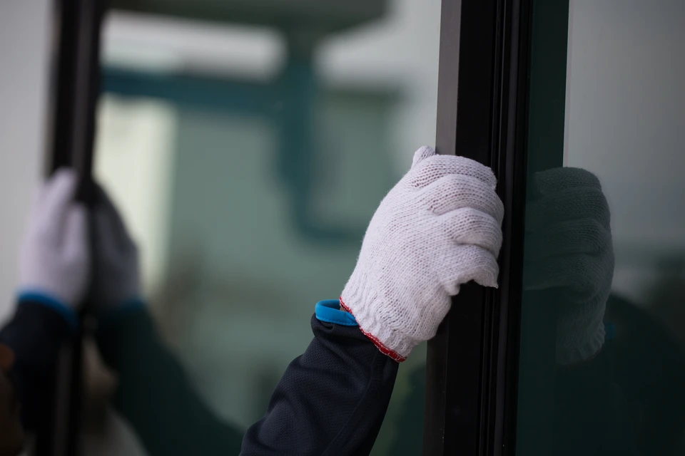 Photographie réaliste en couleur montrant un artisan installer une fenêtre ou un volet aluminium/menuiserie extérieure sur la façade d'une maison. L'artisan, vêtu professionnellement, utilise des outils adaptés pour poser le produit. La scène se déroule sur un chantier résidentiel en extérieur, montrant clairement le contexte de pose chez un client (particulier ou professionnel). L'image doit transmettre la qualité, la propreté et le professionnalisme du chantier.