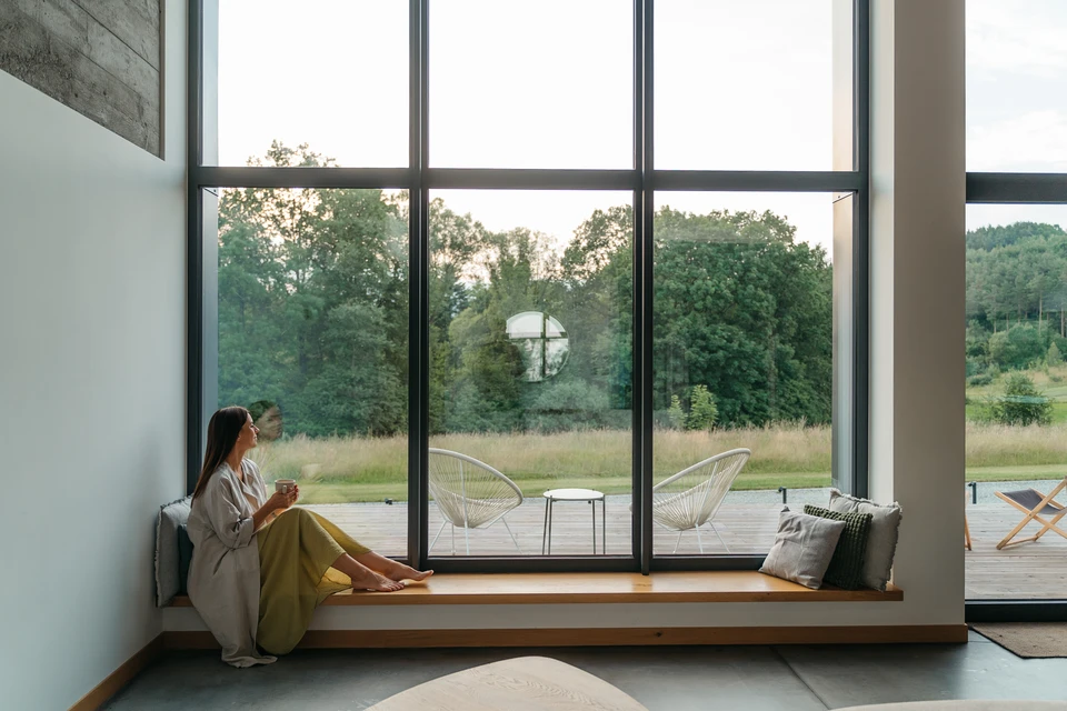 Ouvrier en salopette bleue et casquette installant une fenêtre coulissante sur façade extérieure d'habitation