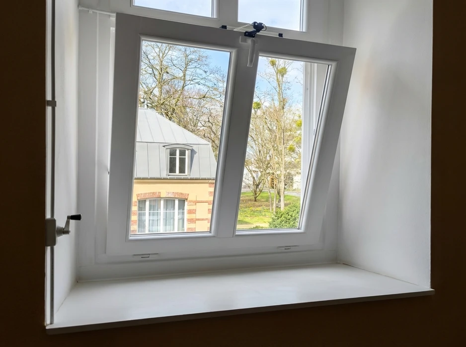 Deux ouvriers en uniformes bleu marine et casques blancs installent une fenêtre PVC double battant dans un mur intérieur blanc